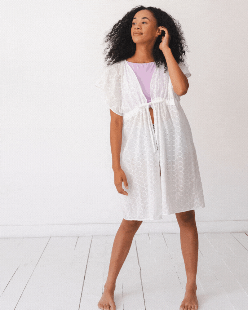 GIF of a woman wearing a white kaftan cover-up and a lilac swim crop top