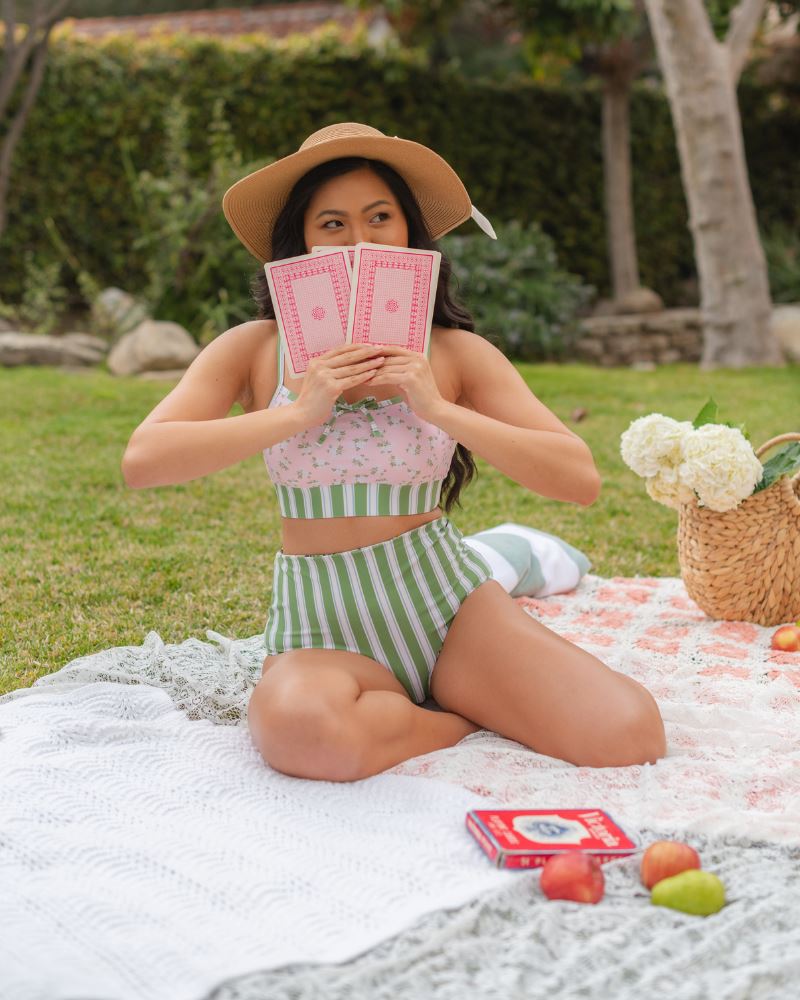 Photo of a woman posing outside wearing a pink and green floral swim bralette and a white and pink floral/ green striped reversible swim bottom- striped side