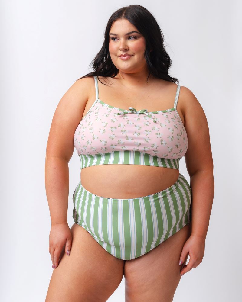 Photo of a woman wearing a pink and green floral swim bralette and a white and pink floral/ green striped reversible swim bottom- striped side