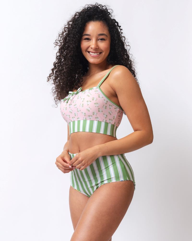 Photo of a woman wearing a pink and green floral swim bralette and a white and pink floral/ green striped reversible swim bottom- striped side- side angle