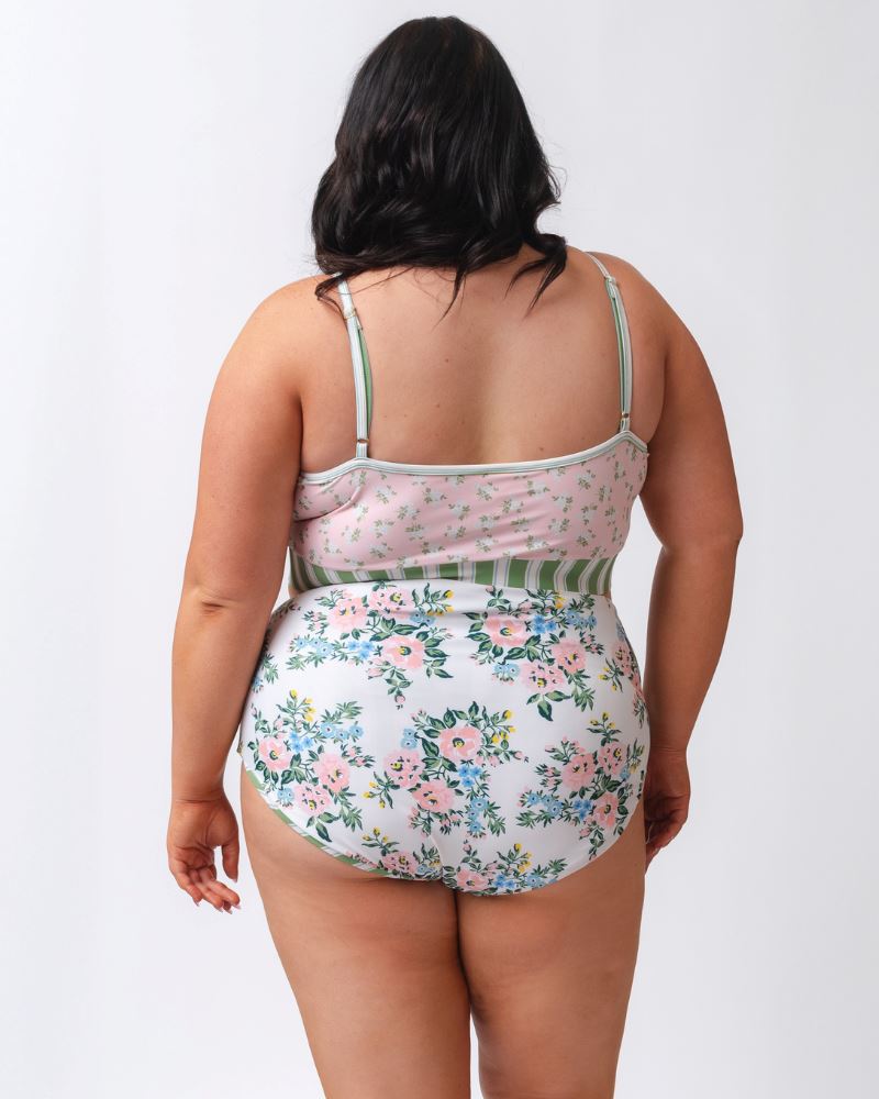 Photo of a woman wearing a pink and green floral swim bralette and a white and pink floral/ green striped reversible swim bottom- floral side- back angle