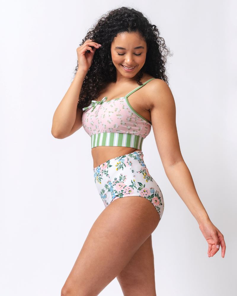 Photo of a woman wearing a pink and green floral swim bralette and a white and pink floral/ green striped reversible swim bottom- floral side- side angle