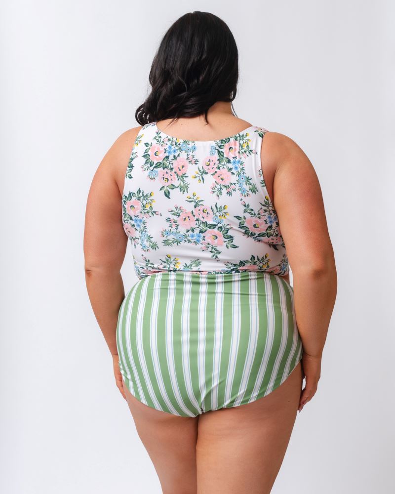 Photo of a woman with her back facing us wearing a pink and white floral cropped swim top with green and white striped high waist swim bottoms