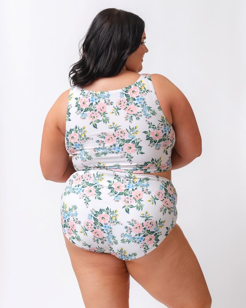 Photo of a woman with her back facing us wearing a pink and white floral cropped swim top with pink and white floral high waist swim bottoms