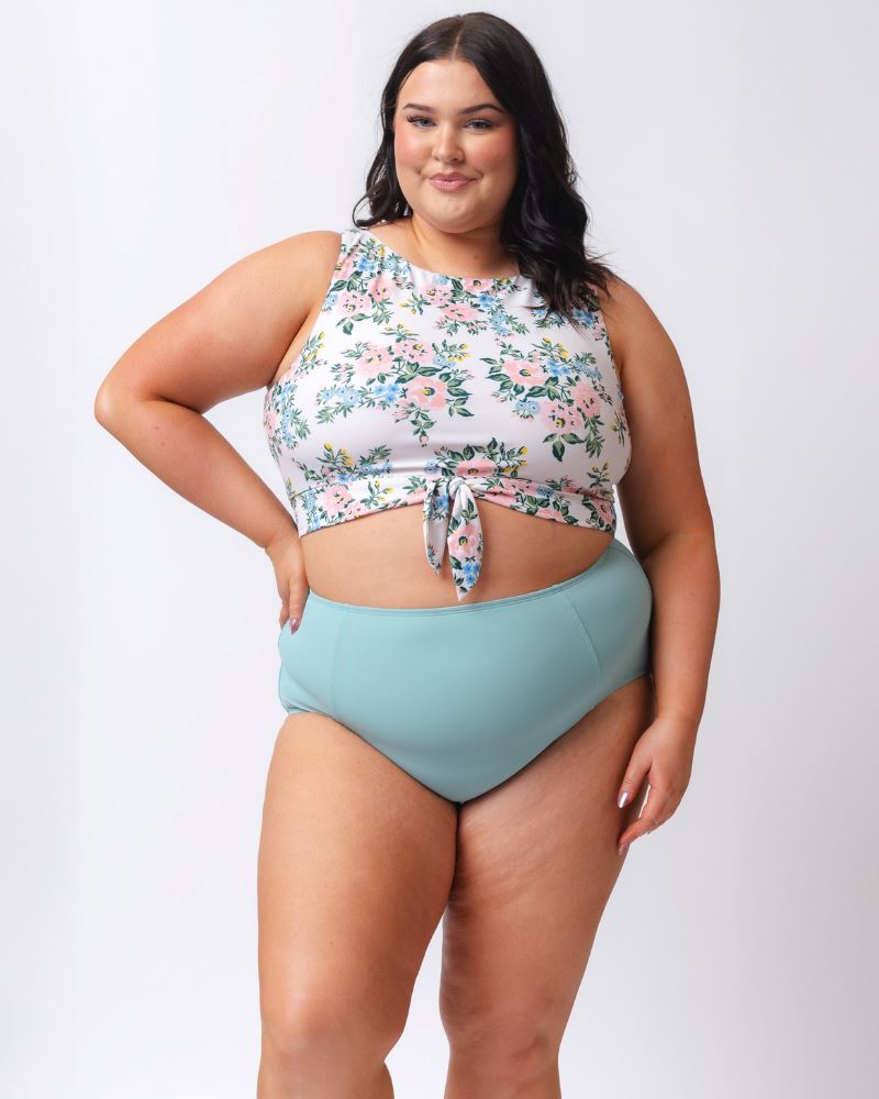 Photo of a woman wearing a light blue high waist swim bottom and a pink and white floral swim crop top