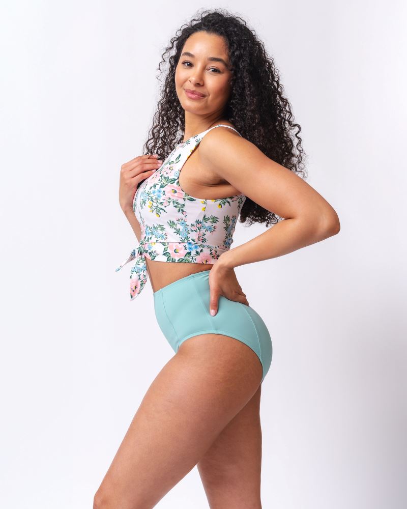 Photo of a woman wearing a light blue high waist swim bottom and a pink and white floral swim crop top- side angle