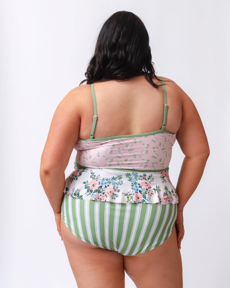 Photo of a woman with her back facing us wearing a pink and white floral swim top with green and white stripe high waist swim bottoms