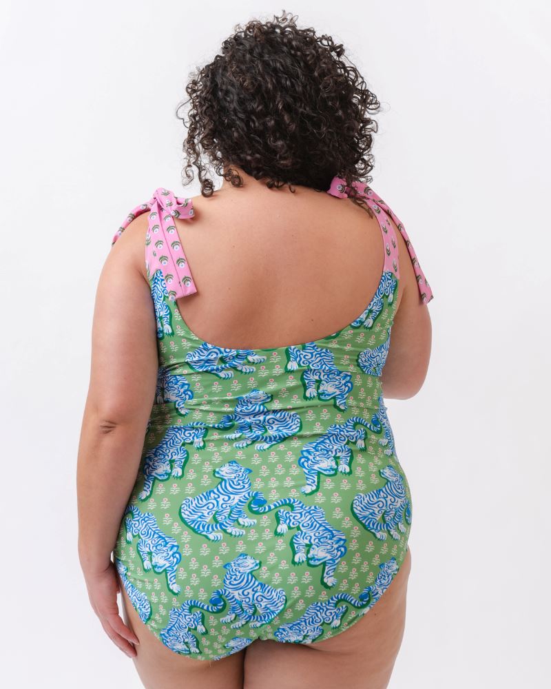 Photo of a woman with her back facing us wearing a bold green and pink tiger print shoulder tie swim one piece