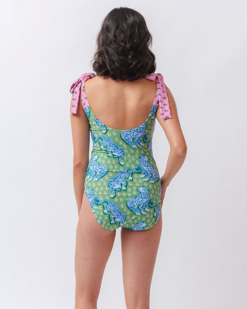 Photo of a woman with her back facing us wearing a bold green and pink tiger print shoulder tie swim one piece