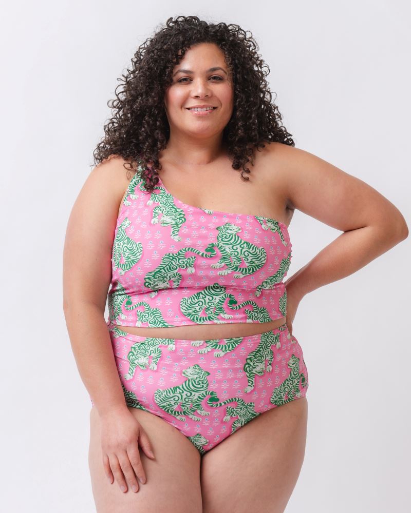 Photo of a woman wearing a bold pink and green tiger print one shoulder crop swim top with matching high waist swim bottoms