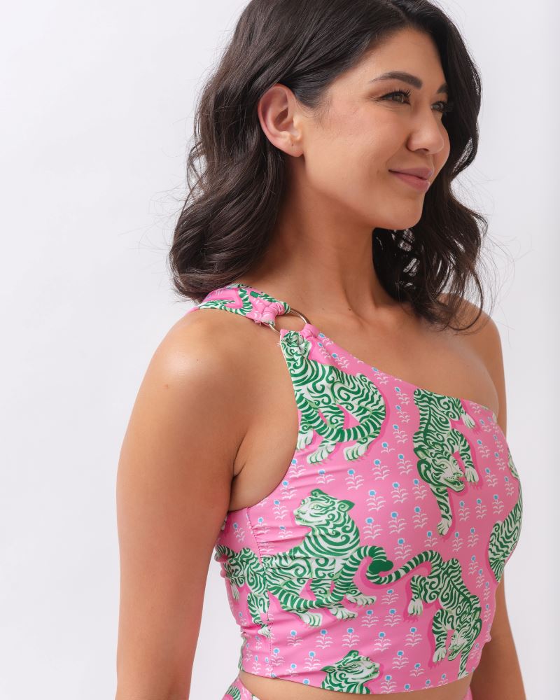 Close up photo of a woman wearing a bold pink and green tiger print one shoulder crop swim top