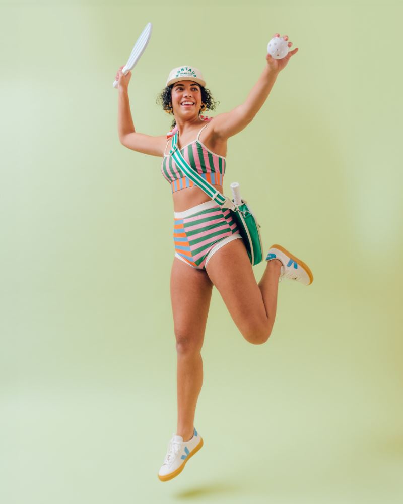 Photo of a woman jumping wearing a multi-colored striped swim bralette and a multi-colored striped retro swim short bottom