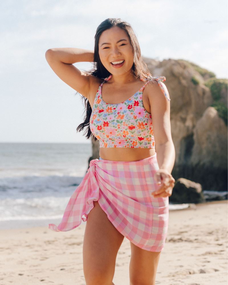 Photo of a woman wearing a pink and white checkered Sarong and a floral swim crop top