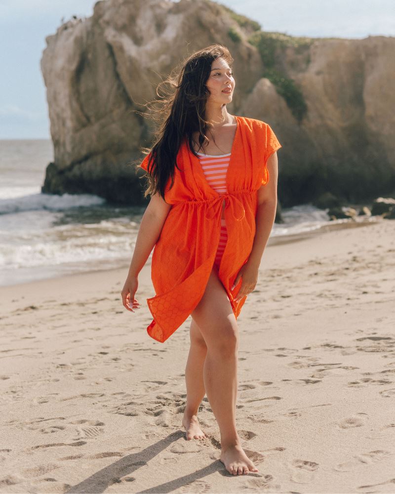 Photo of a woman wearing an orange Kaftan cover up and a pink and orange stripe swim top and a pink and orange stripe swim bottom