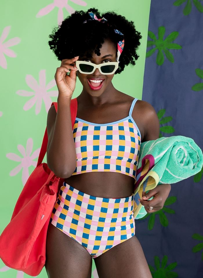 Photo of woman posing with sunglasses while wearing a multi colored checkered cropped swim top with multi colored checkered high waist swim bottoms