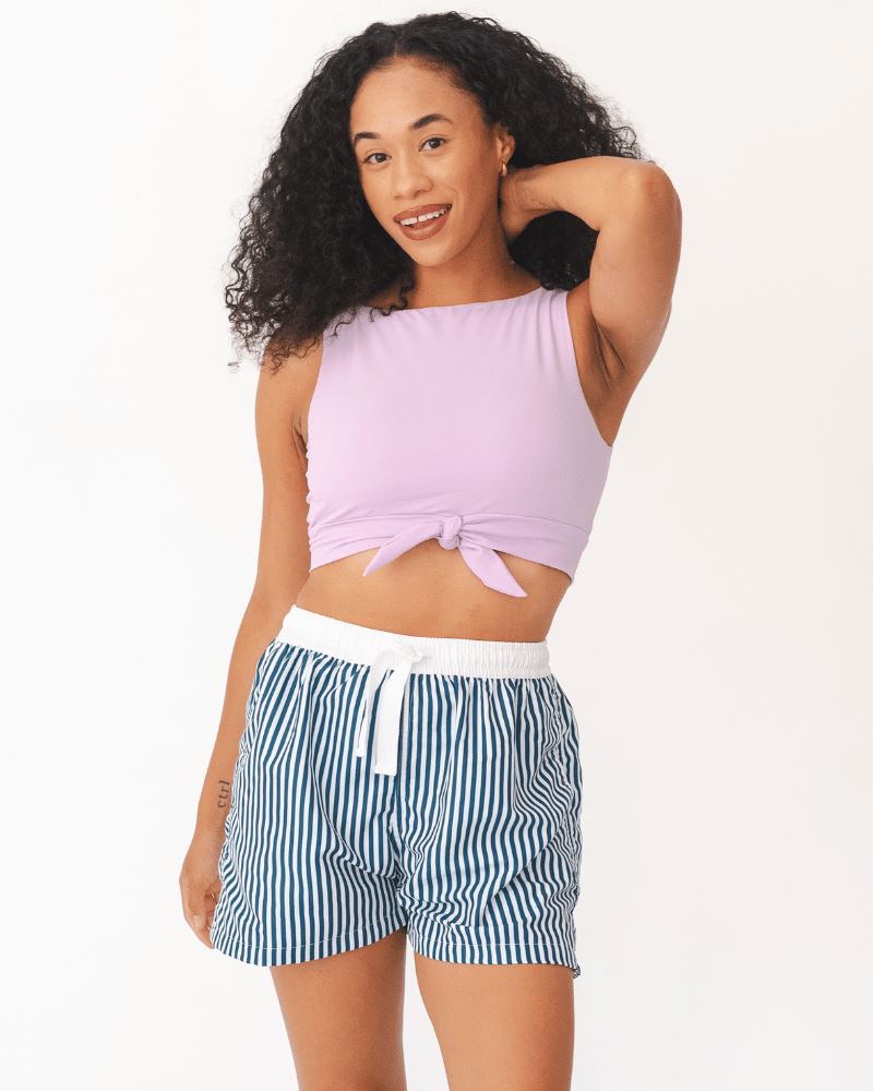 Photo of a woman wearing blue and white stripe swim board shorts and a lilac swim crop top