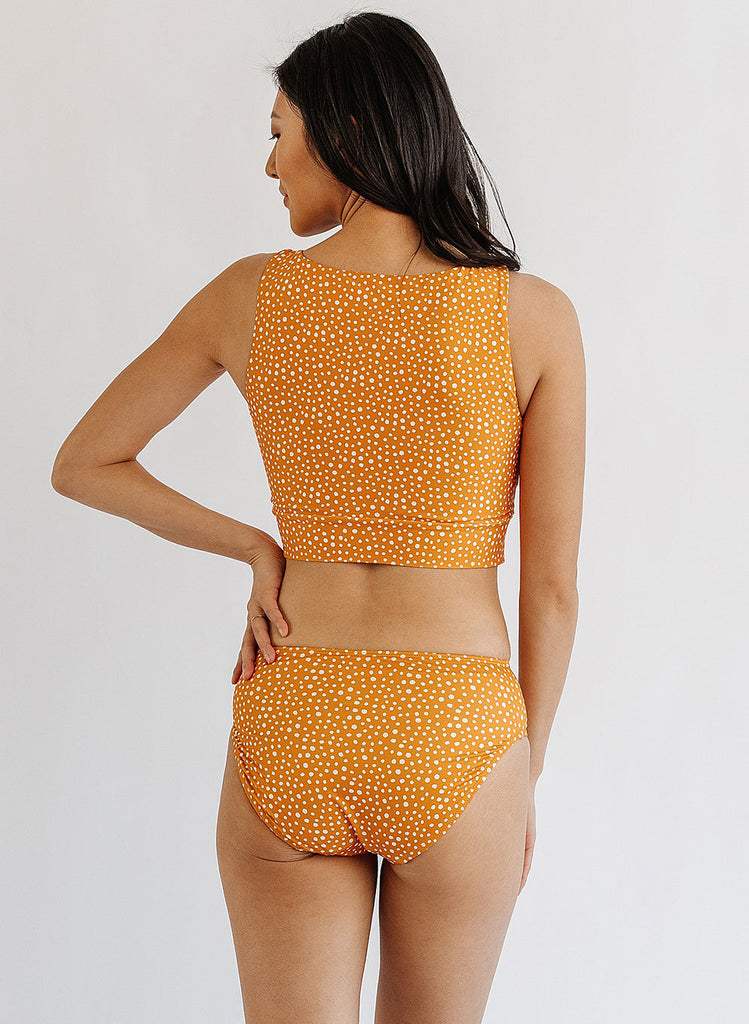 Photo of woman wearing orange and white dot cropped swim top with orange and white dot mid waist bottoms back angle