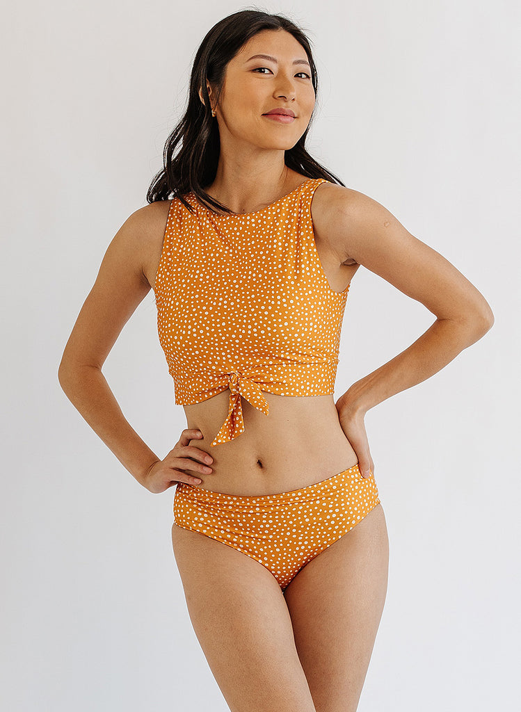 Photo of woman wearing orange and white dot cropped swim top with orange and white dot mid waist swim bottoms