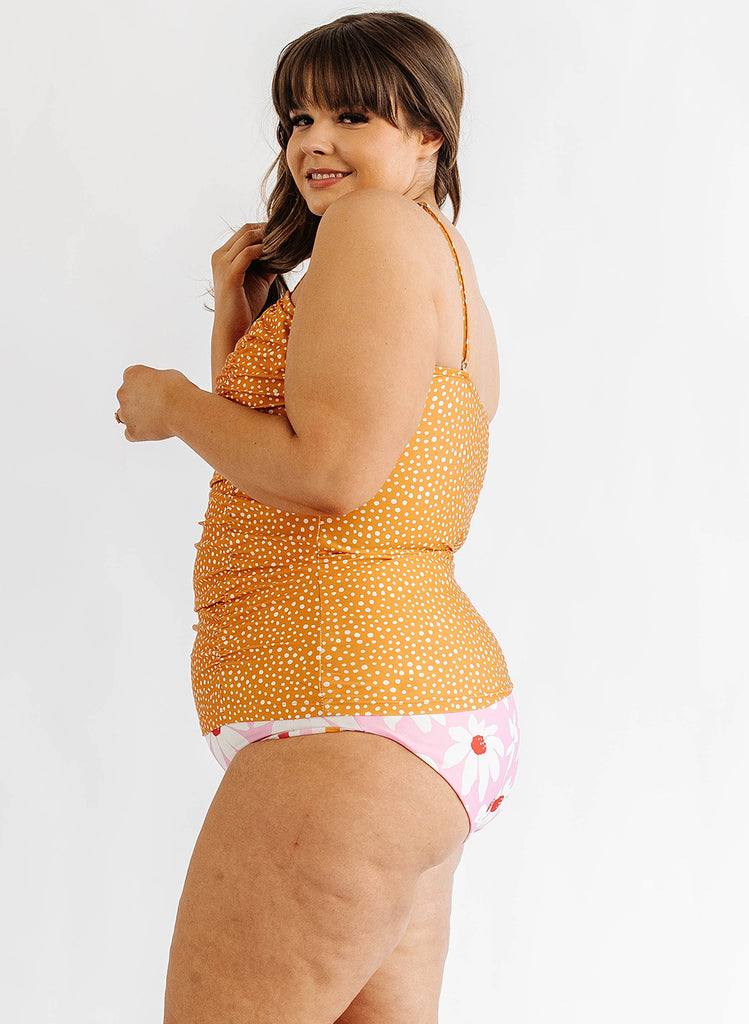 Photo of woman wearing orange and white dot swim tankini with pink floral swim bottoms side angle