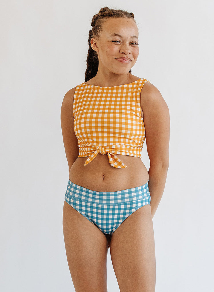 Photo of woman wearing yellow and white gingham cropped swim top with blue and white gingham swim bottoms
