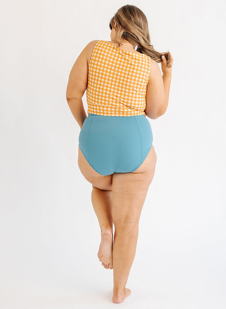 Photo of woman wearing yellow and white gingham cropped swim top with blue swim bottoms back angle