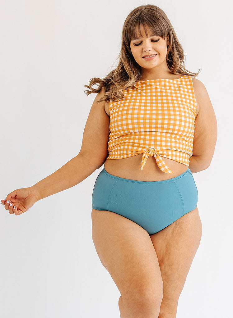 Photo of woman wearing yellow and white gingham cropped swim top with blue swim bottoms