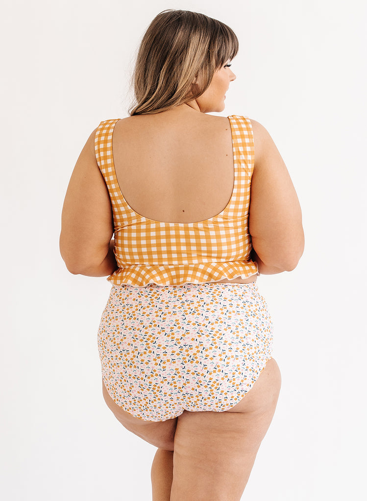 Photo of woman wearing yellow and white gingham swim top with multi color floral swim bottoms back angle