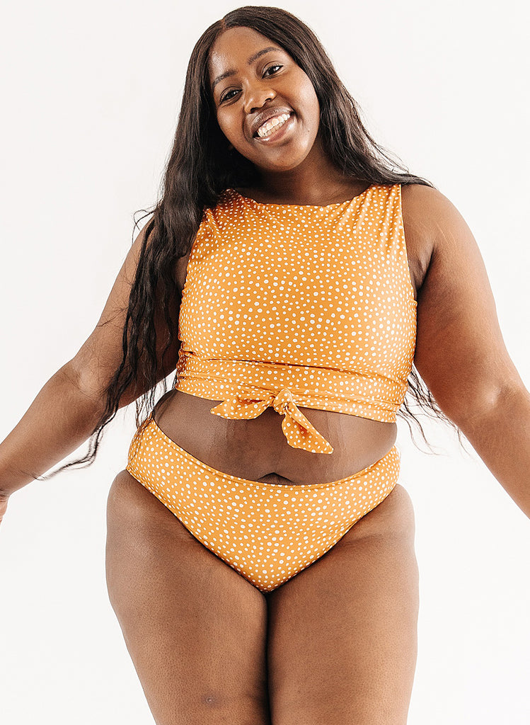 Photo of woman wearing orange and white dot cropped swim top with orange and white dot mid waist swim bottoms