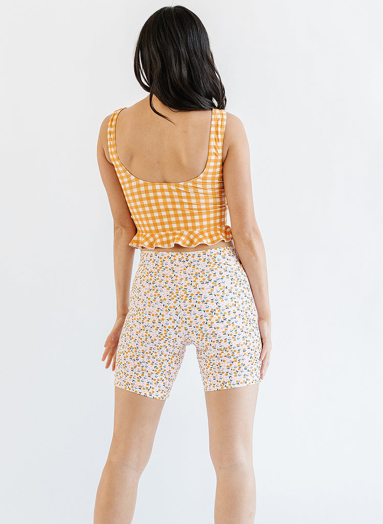 Photo of woman wearing yellow and white gingham swim top with multi color floral long swim shorts back angle