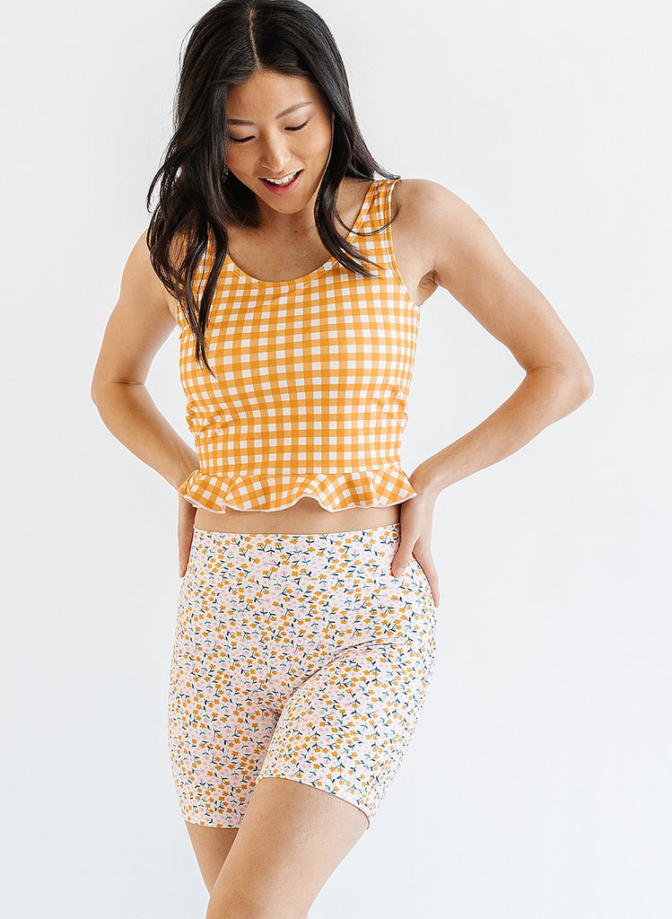 Photo of woman wearing yellow and white gingham swim top with multi color floral long swim shorts