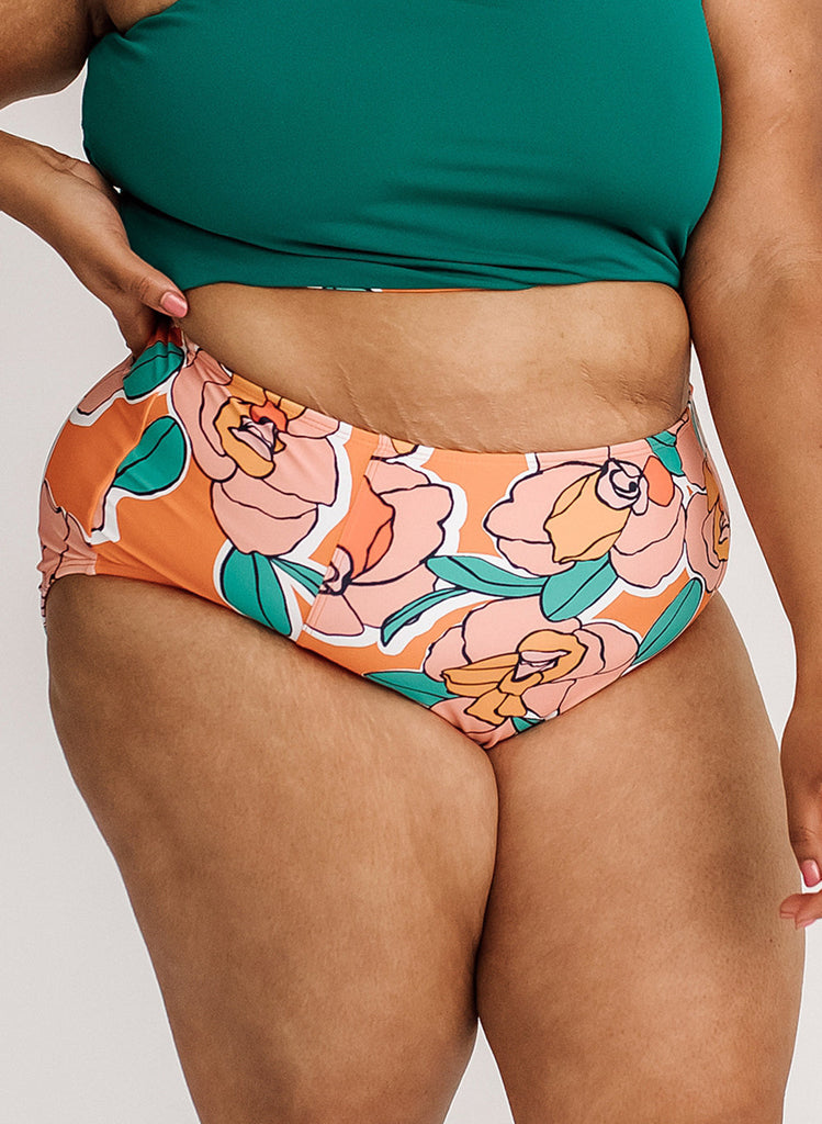 Close up photo of a woman wearing a blue cropped swim top with orange floral high waist swim bottoms