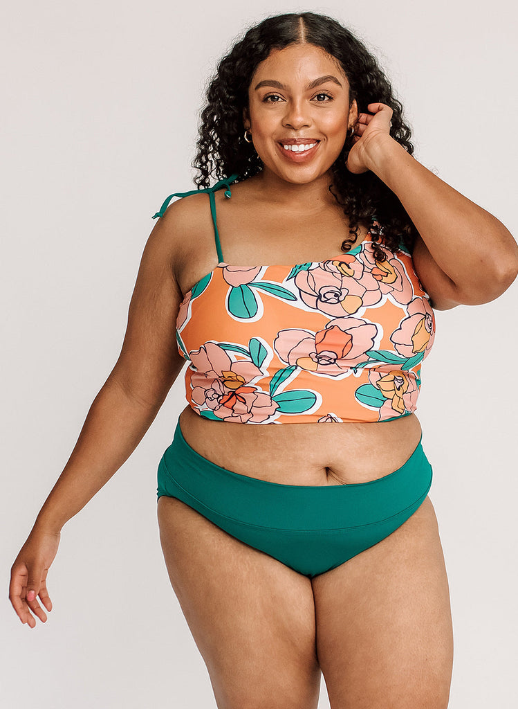 Photo of a woman wearing an orange floral cropped swim top with blue classic low rise swim bottoms