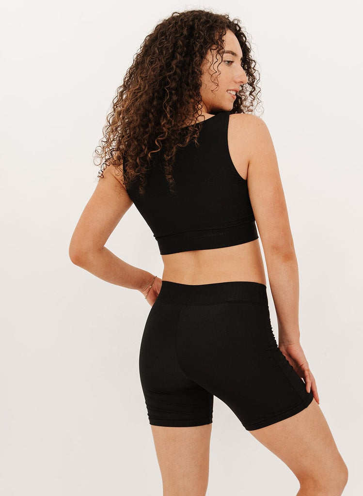 Photo of a woman in black mid thigh swim shorts and a black knotted swim crop top from the back