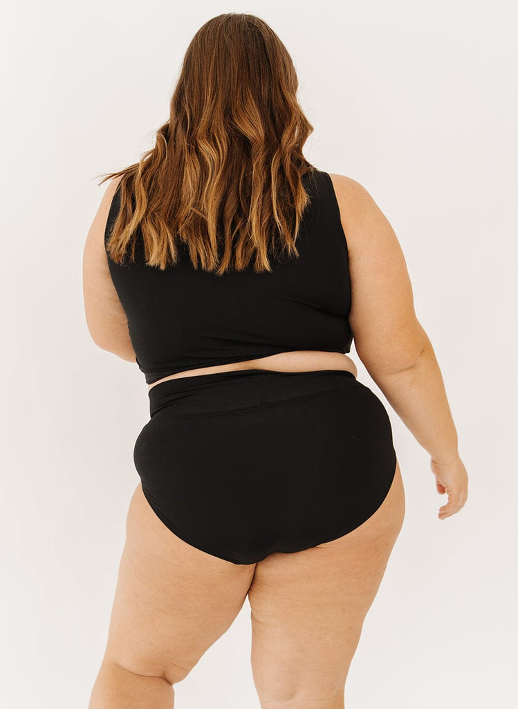 Photo of a woman in black classic swim bottoms and black swim crop top back angle