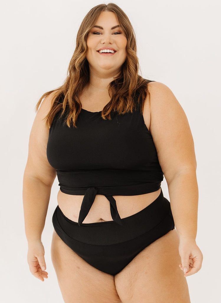 Photo of a woman wearing a black knotted crop swim top with black high-waist swim bottoms