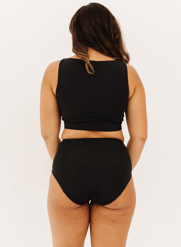 Photo of a woman wearing black high-waist swim bottoms with a black knotted crop swim top back angle