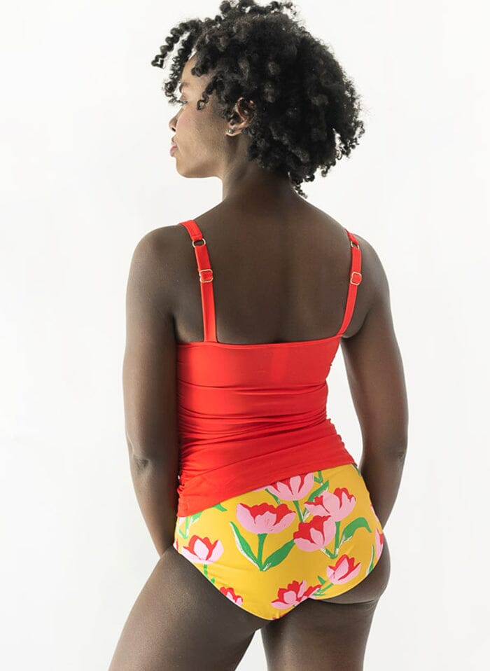 Photo of a woman wearing a red square-neck swim top and a yellow floral swim bottom back angle