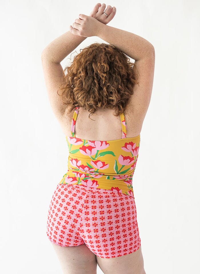 of a woman wearing a Claus square-neck swim top and a floral swim short bottom back angle