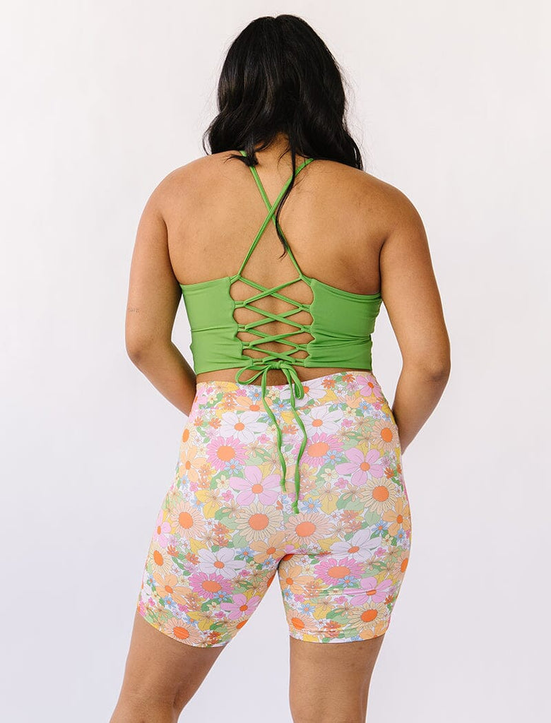 Photo of woman wearing green cropped lace back swim top with multi colored long swim shorts back angle
