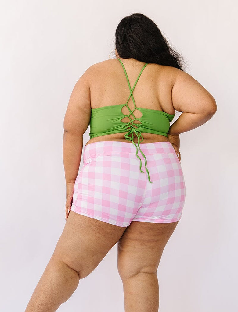 Photo of woman wearing green cropped lace back swim top with pink gingham swim shorts back angle