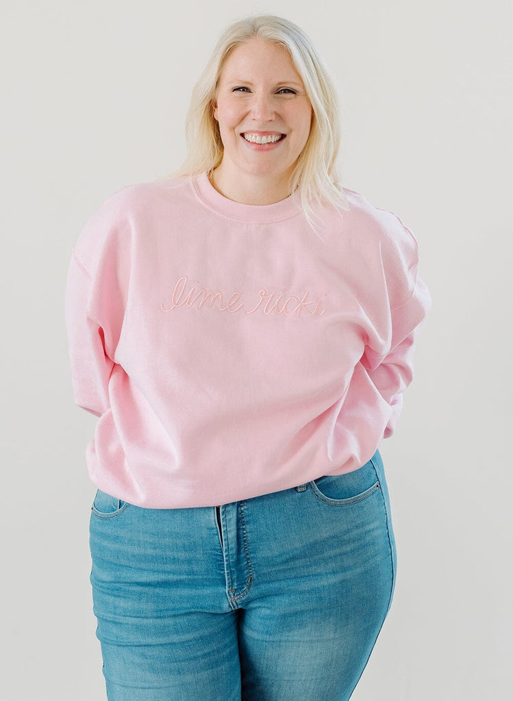 Photo of a woman wearing a pink crew neck sweatshirt and blue jeans