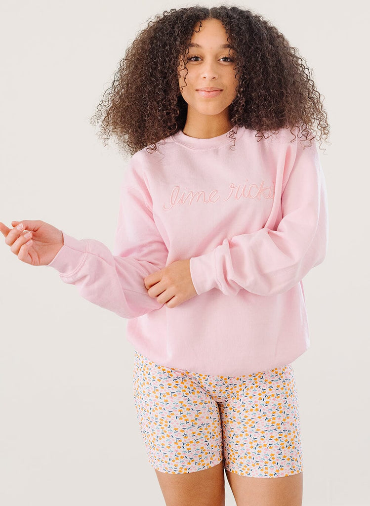 Photo of a woman wearing a pink crew neck sweatshirt and a multi color floral swim short
