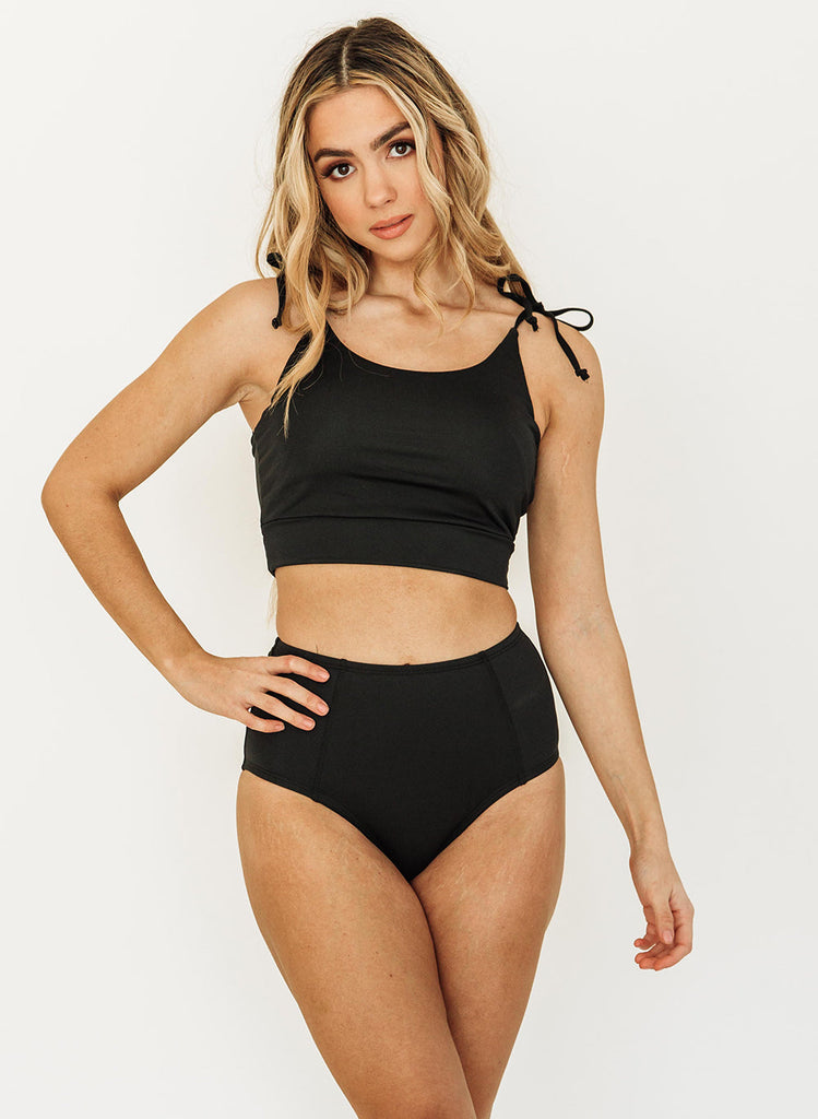 Photo of a woman wearing a black shoulder-tie swim crop top and a black swim bottom