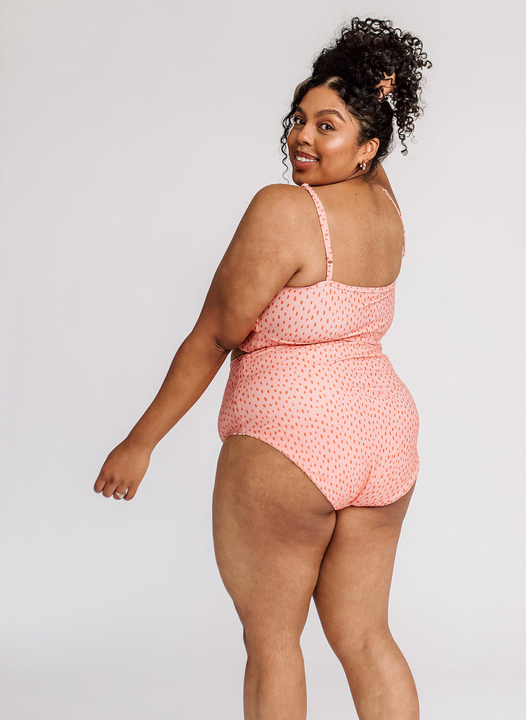 Photo of a woman wearing a pink dotted swim bralette and a pink dotted swim bottom- side/ back angle