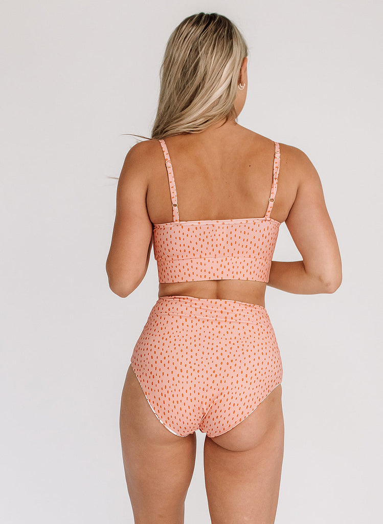 Photo of a woman with her back facing us wearing a pink polka dot cropped swim top with pink polka dot high waist swim bottoms