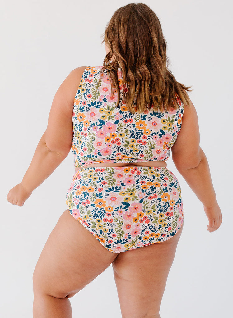 Photo of a woman with her back facing us wearing a multi colored floral cropped swim to with multi colored floral high waist swim bottoms