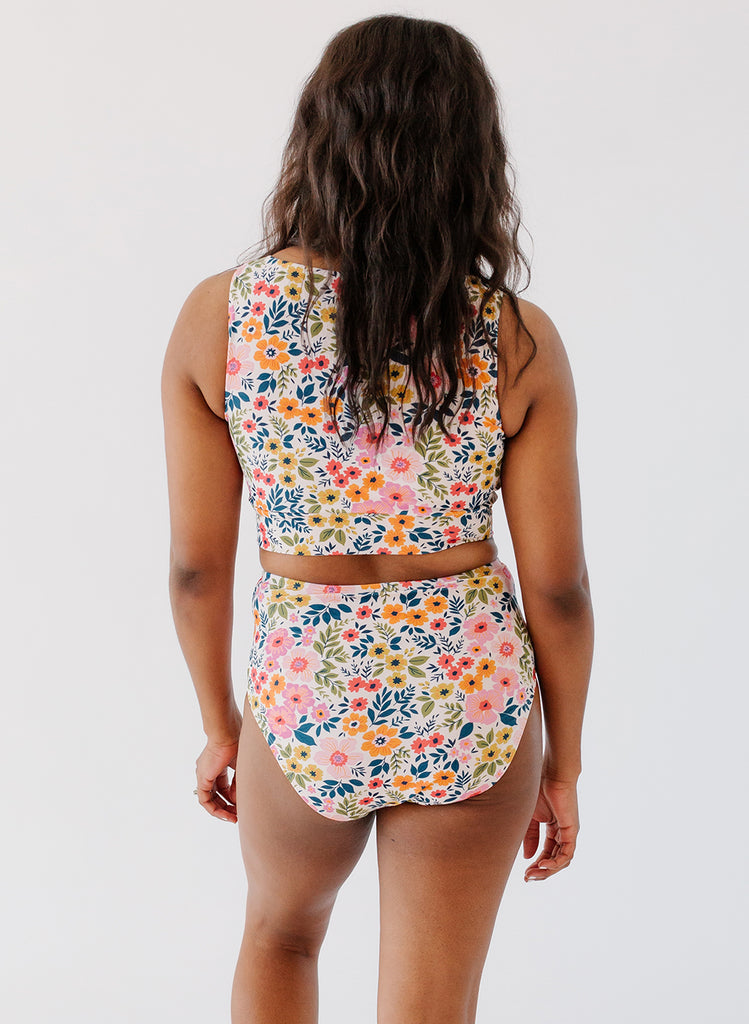 Photo of a woman with her back facing us wearing multi colored floral cropped swim top with multi colored floral high waist swim bottoms