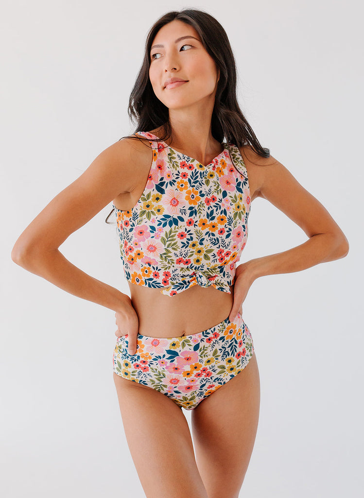 Photo of a woman with her hands on her hips wearing a multi colored floral cropped swim top with multi colored floral high waist swim bottoms