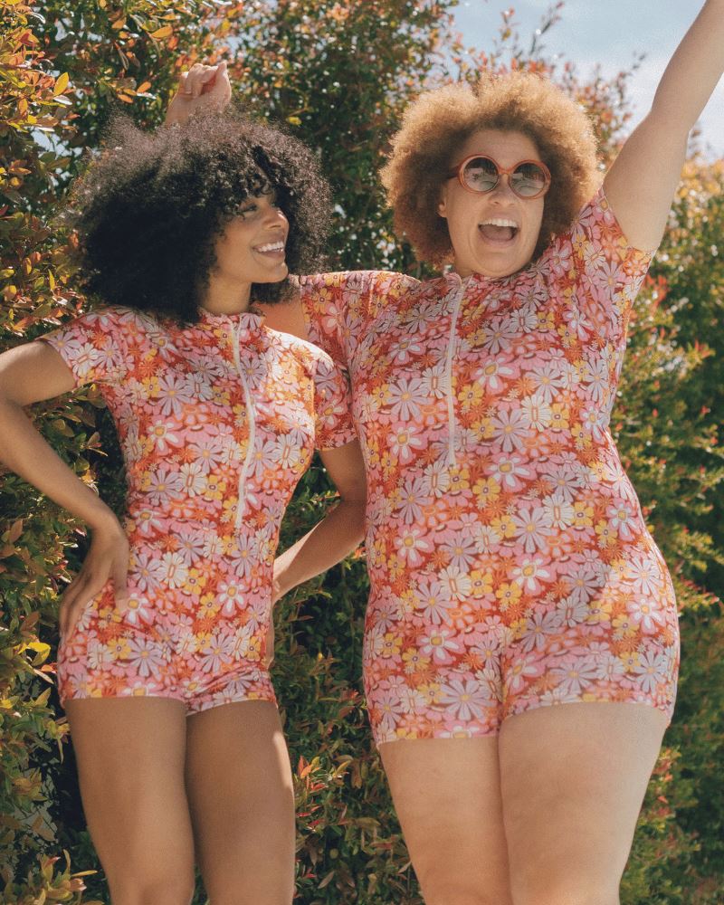 Photo of two women wearing a groovy Blooms floral rash guard one-piece swim suit