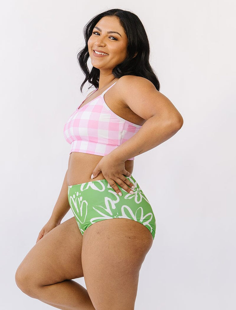 Photo of woman wearing pink gingham bralette swim top with green and white floral swim bottoms side angle